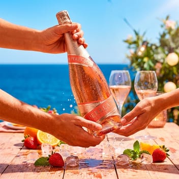 Бутилка Perelada Rosé Festival, подавана от ръка на ръка над лятна маса