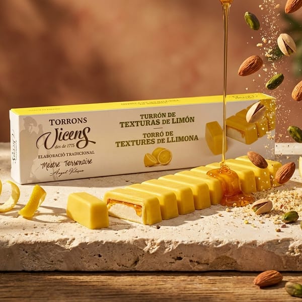 Кутия турон Texturas de Limón на Torrons Vicens върху варовиков плот, с нарязани жълти блокчета, разрязан лимон и струя мед в следобедно слънце
