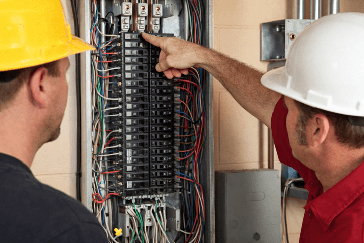 two men with contruction caps poiting to main electric unit