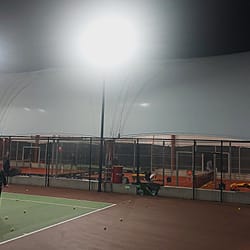 Διαγώνια εξωτερική άποψη της εφελκυόμενης μεμβρανικής κατασκευής με ασύμμετρη καμάρα, που καλύπτει γήπεδο πάντελ.